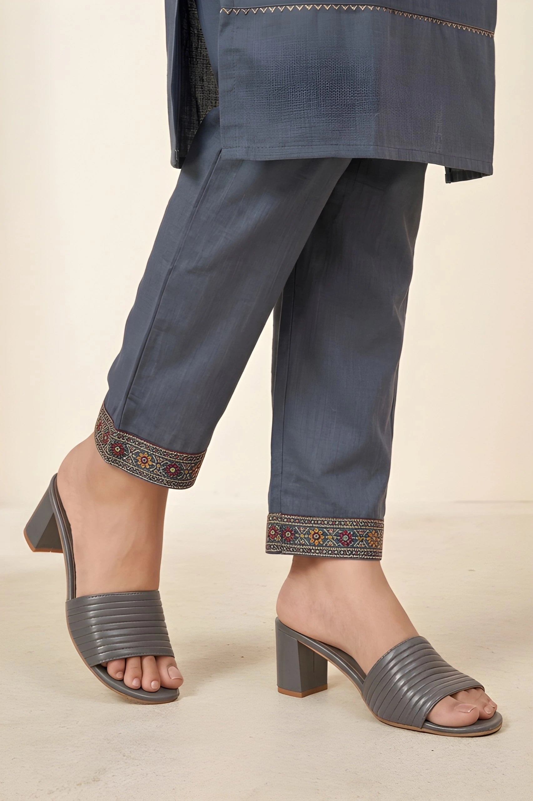 Navy blue pants with embroidered cuffs worn by a person on a beige background